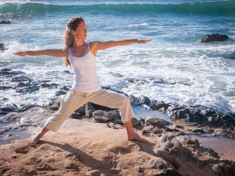 A woman with loose yoga pants doing yoga at the beach.