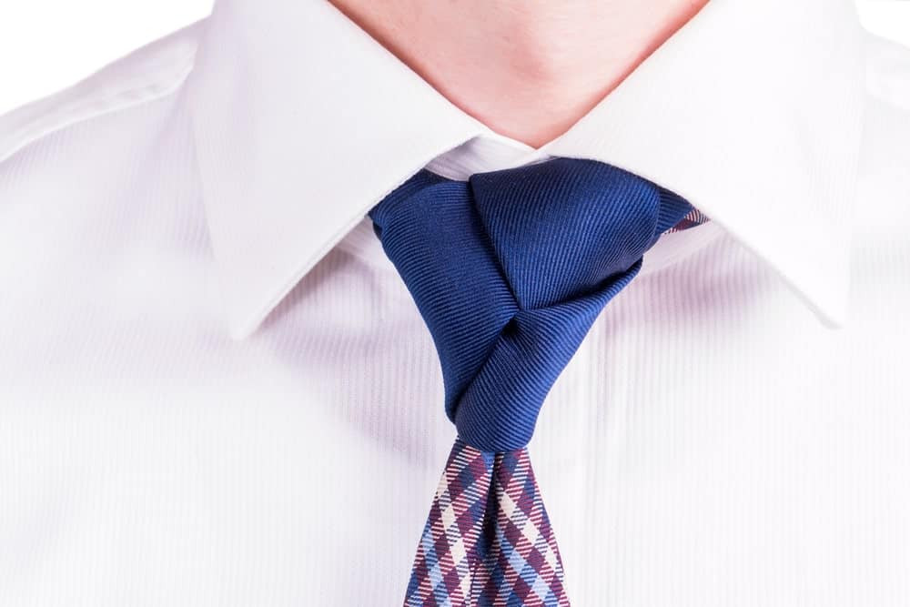 Blue necktie with Trinity tie knot on a white long sleeve.