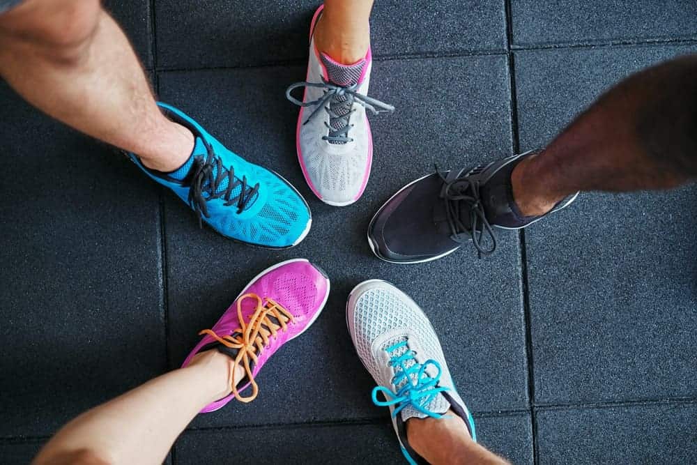 A look at various running shoes on a dark tiled floor.