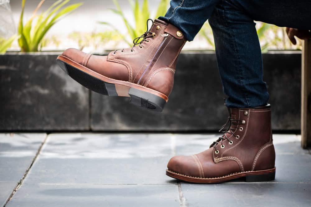 This is a close look at a man wearing a pair of brown leather boots with his jeans.