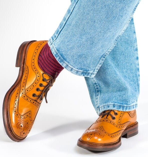 This is a close look at a man wearing a pair of brogue shoes with his jeans.