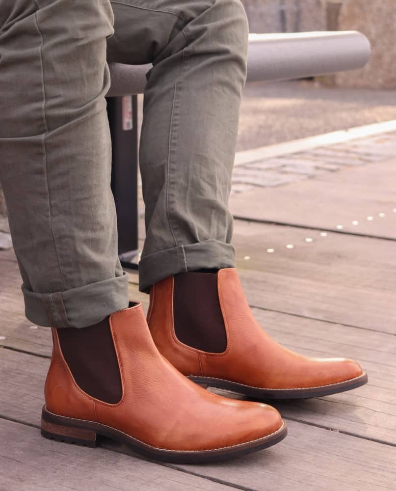A man wearing a pair of brown leather Chelsea boots with his jeans.