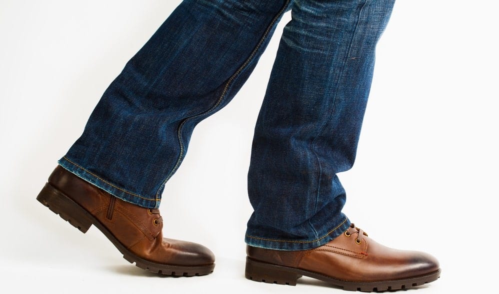 A close look at a man wearing brown leather walking shoes with his jeans.