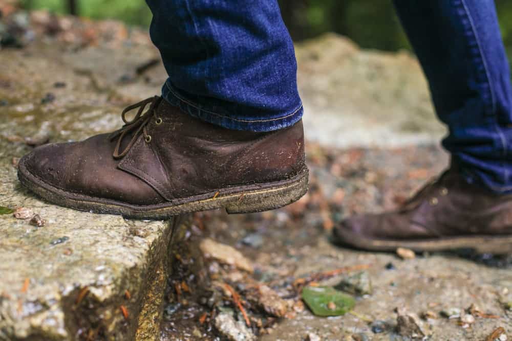 A close look at a man wearing dark brown chukka shoes with his jeans.