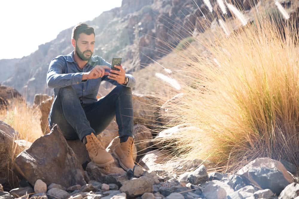 A man sitting on a rock wearing a pair of jeans and desert boots.