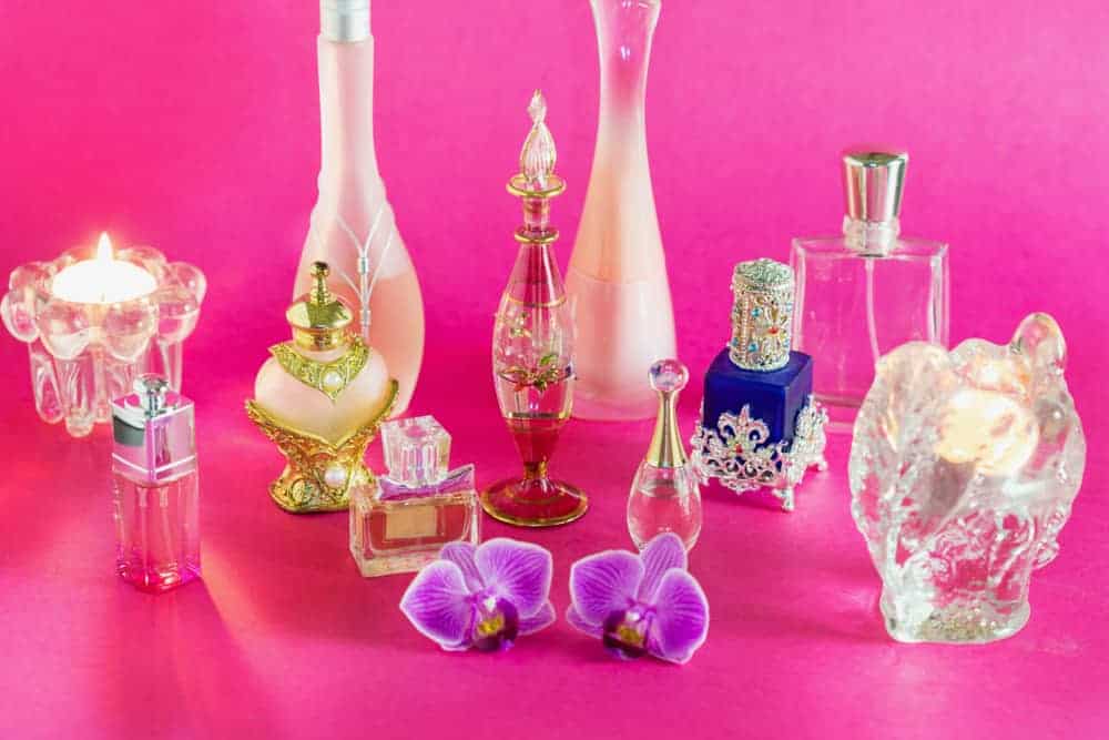Perfume bottles with orchid flowers against a pink background.