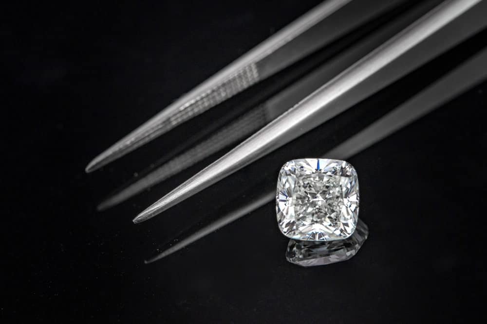 A cushion cut diamond stands out against the tweezers and dark surface.