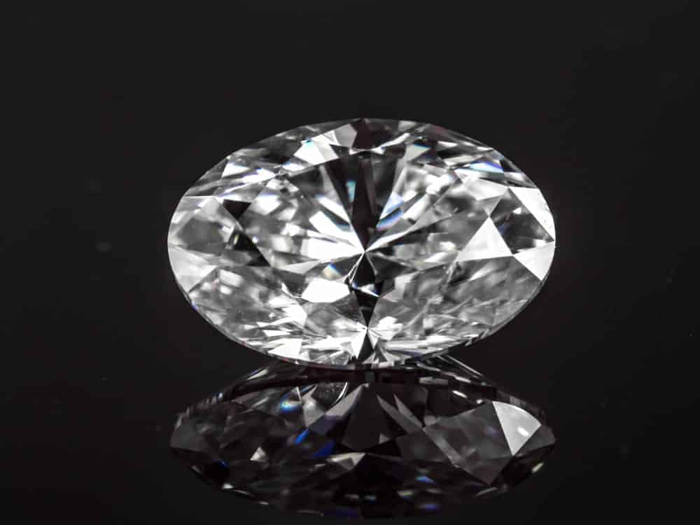This is a close look a pice of oval cut diamond against a dark surface,