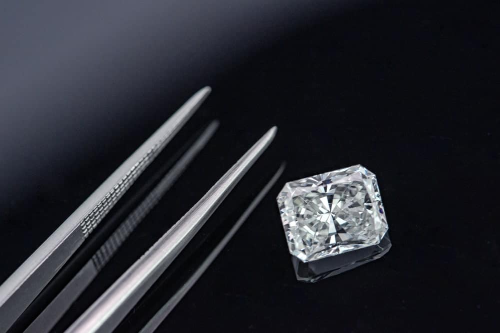 This is a close look at a radiant cut diamond on a dark surface with a pair of tweezers.