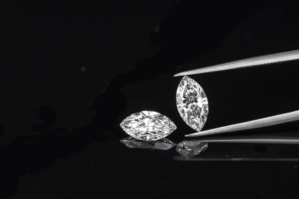 A pair of marquise cut diamonds against a dark surface with a pair of tweezers.