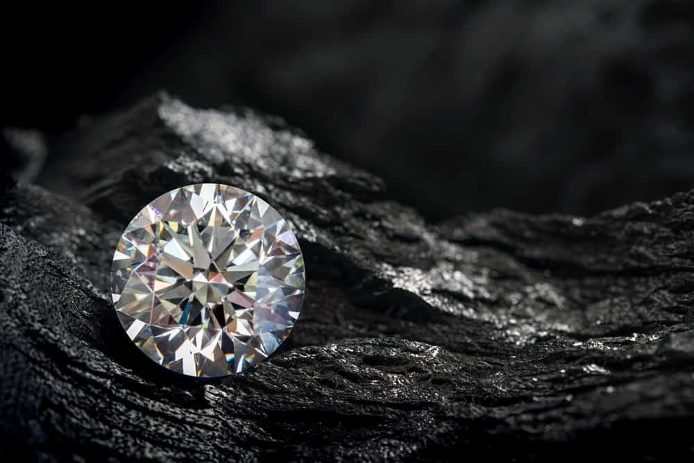 A close look at a round cut diamond against a black coal background.