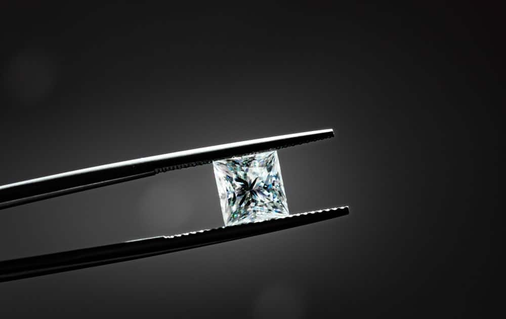 This is a close look at a princess cut diamond held with a pair of tweezers.