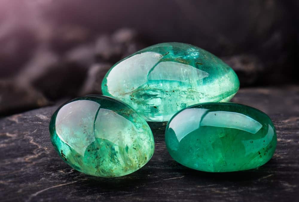 This is a close look at a few emeralds on a dark surface.