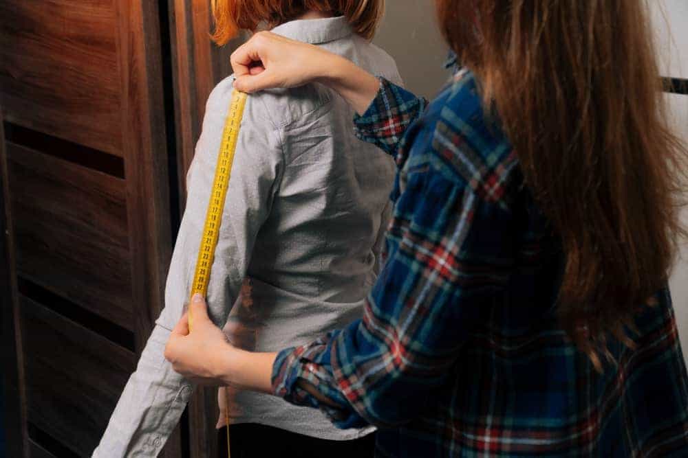 A close look at a seamstress measuring the sleeve of a woman.
