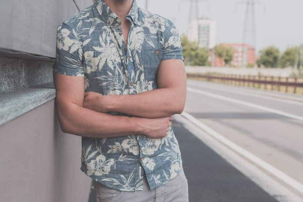 This is a close look at a man wearing a button-down Hawaiian shirt that has short sleeves.