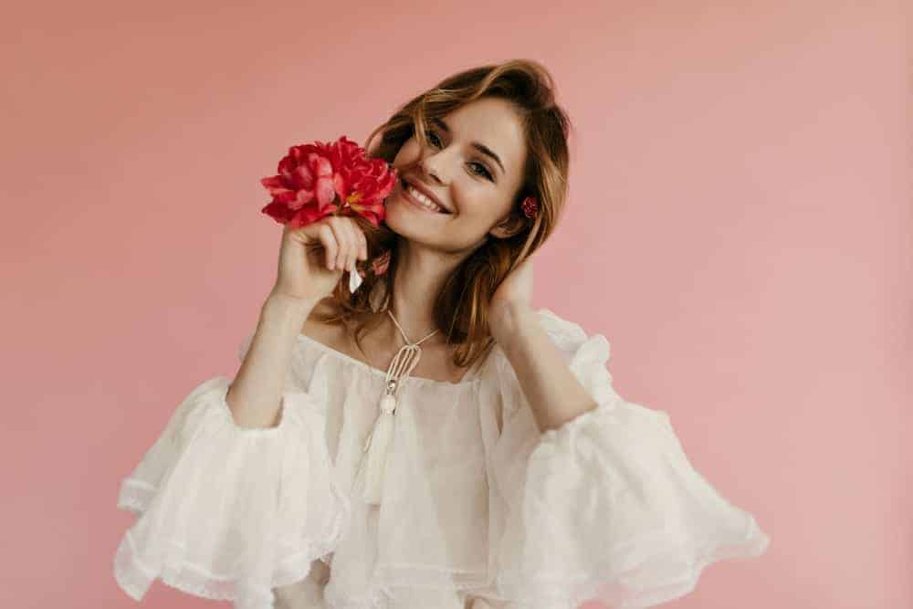 A fashionable woman wearing a white sheer blouse that has angel sleeves.