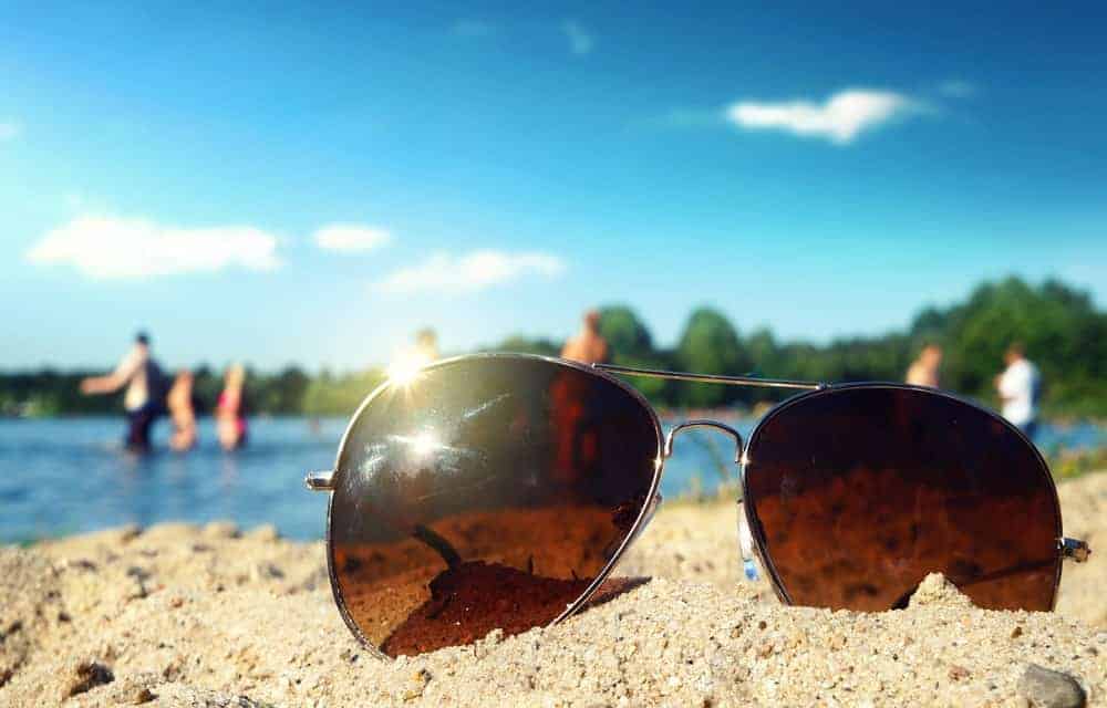A pair of fashionable sunglasses with tinted lenses on the beach sand.