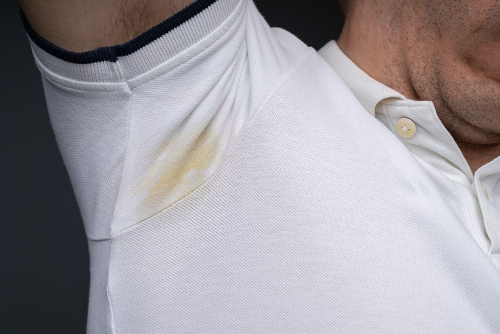 This is a close look at a man wearing a white shirt with pit stains.
