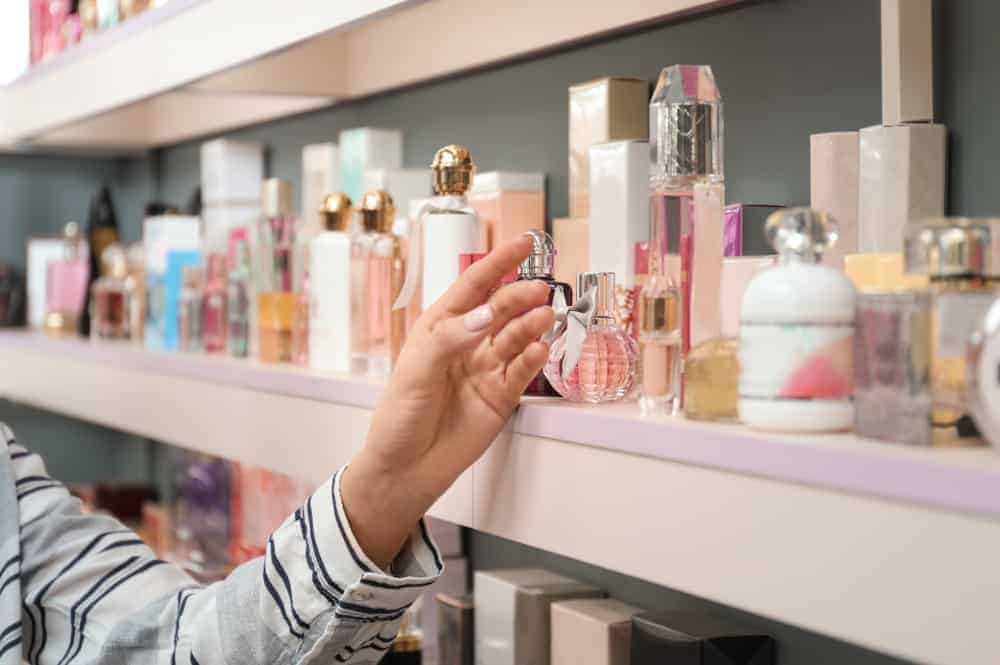Woman picking out a perfume on a display shelf.