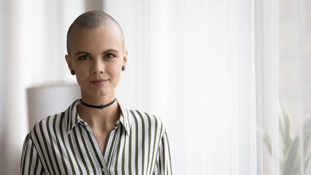 Woman with shaved hair wearing a striped polo blouse.