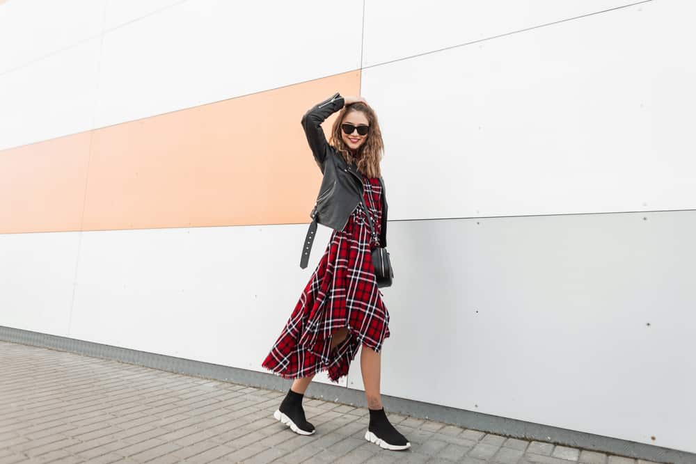 Woman in a red checkered casual dress, sunglasses, and a crossbody bag walking on the street.