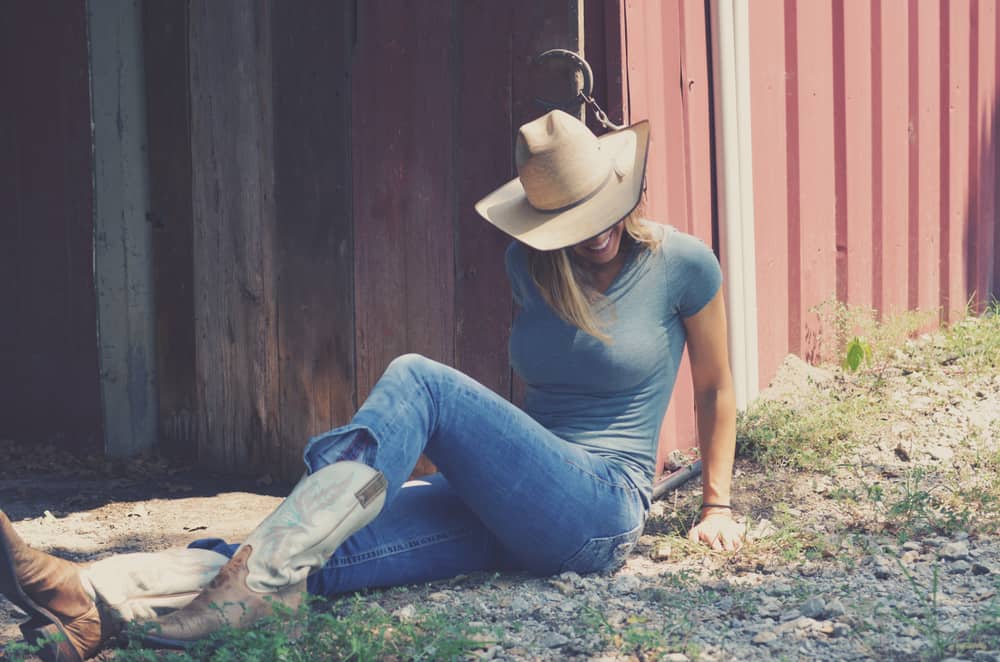 Cowgirl sitting outside a rustic barn.