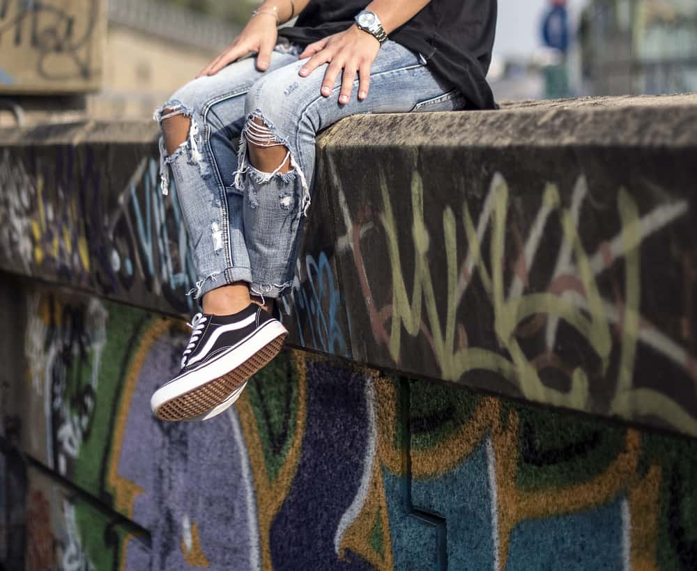 A man wearing a pair of Vans sneakers with his ripped jeans.