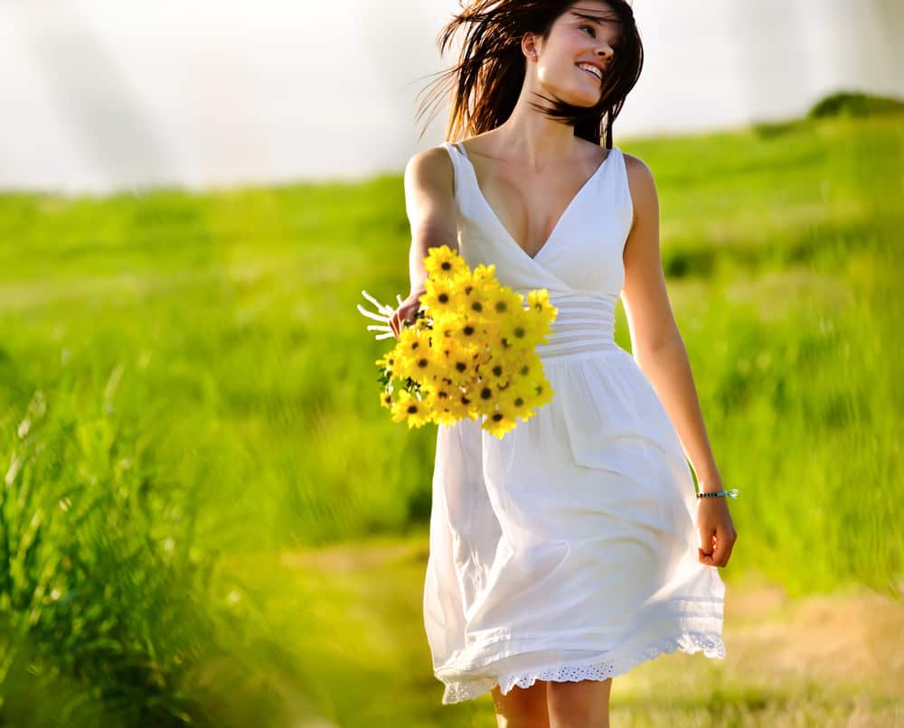 A woman wearing a white summer dress walking at a field of grass.