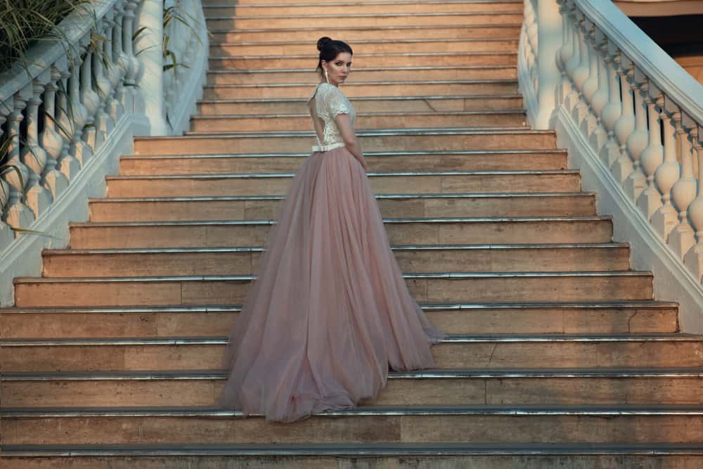 Woman in a ballroom dress walking up the stairs of a palace.