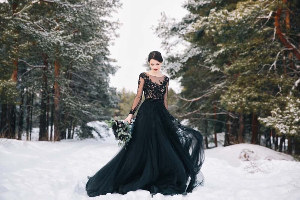 A bride wearing a black wedding dress in a wintry forest.