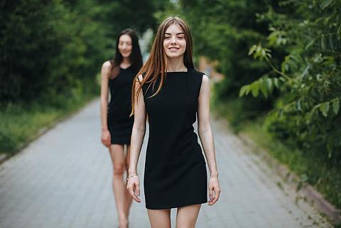 A couple of women walking down the street wearing little black dresses.