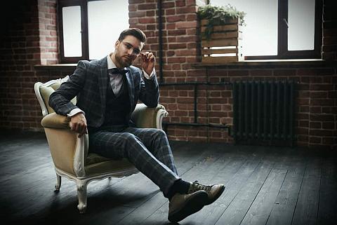 Man in classic suit and glasses sitting on a vintage chair.