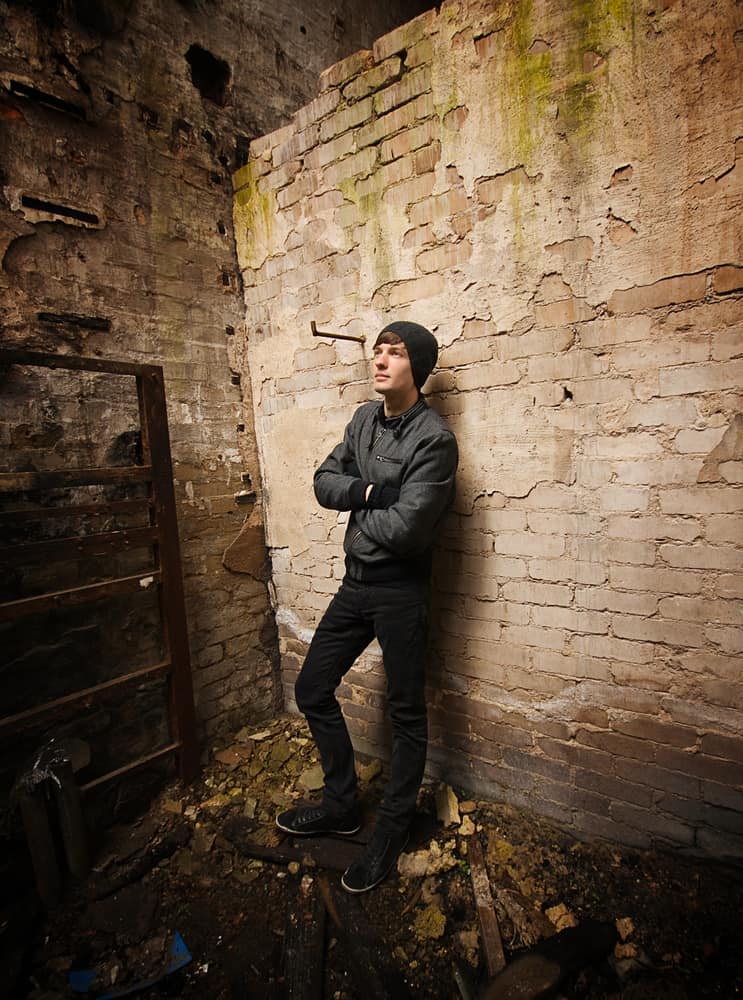 A teen boy with beanie, black jacket, and pants standing in an abandoned area.