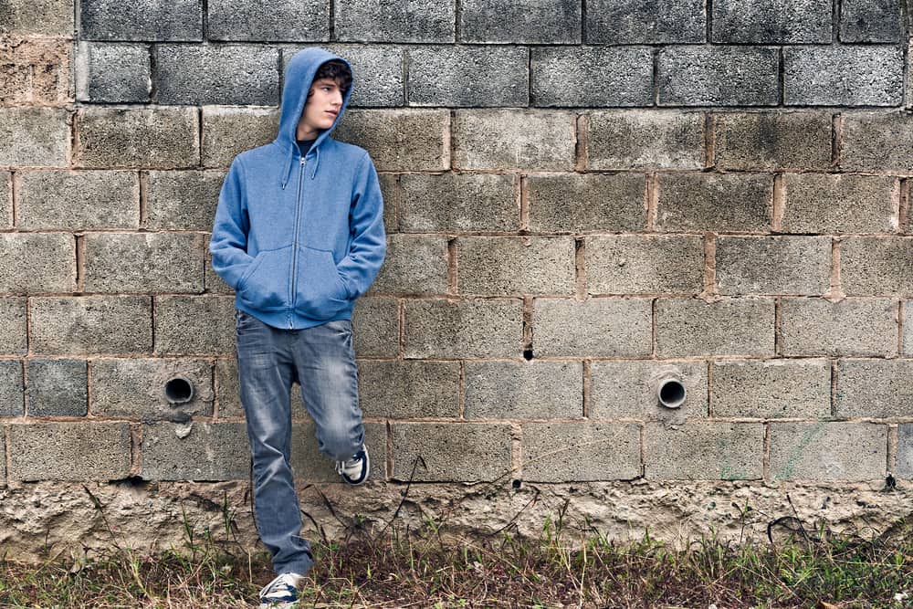 Teen in a hoodie standing against a brick wall.