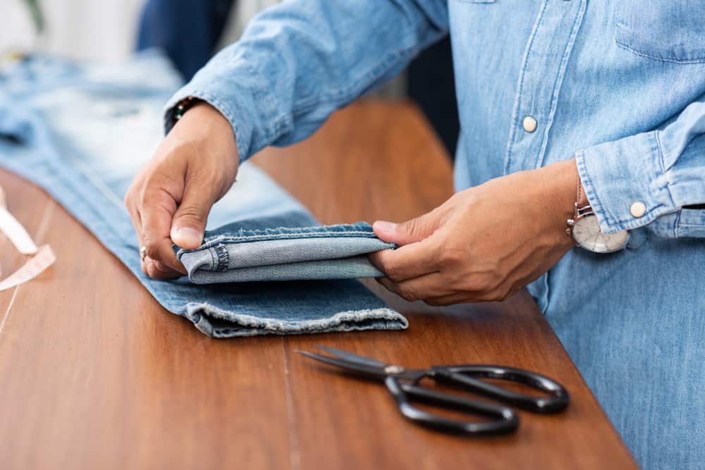 This is a close look at a tailor working on the hem of a pair of jeans.