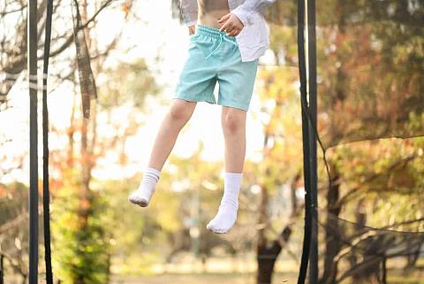 A boy jumping on the trampoline wearing a pair of blue shorts and socks.