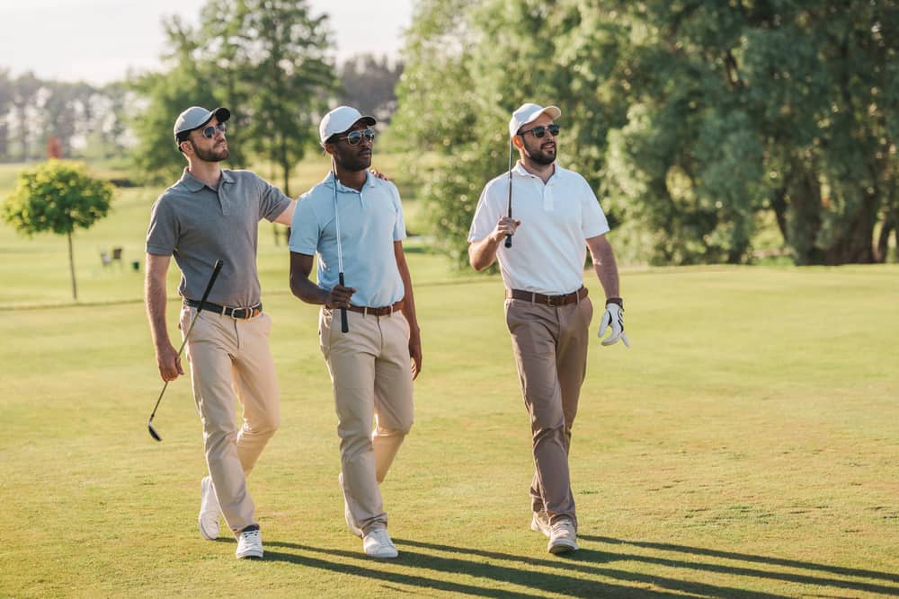 Men in caps and sunglasses holding golf clubs as they walk on the lawn.