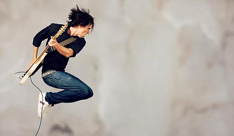 A rocker jumps while playing his guitar.