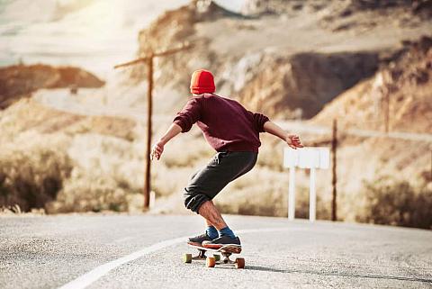 Skateboarder rides by mountain road.
