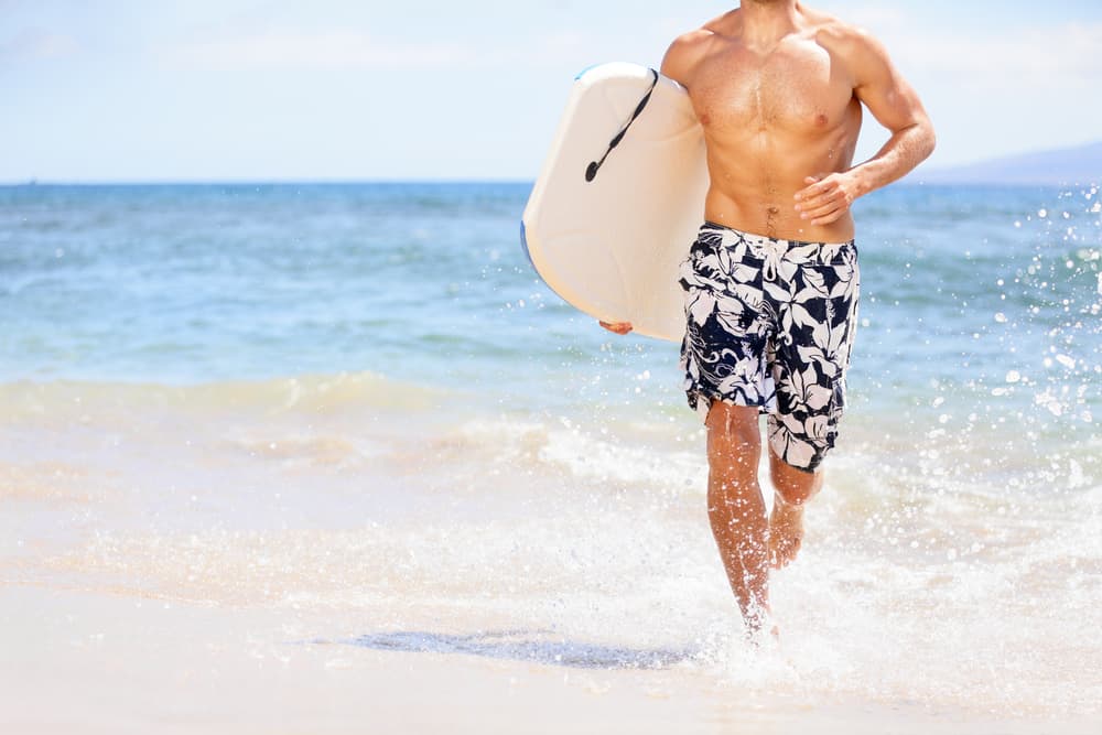 This is a surfer at the beach wearing a pair of floral print board shorts.