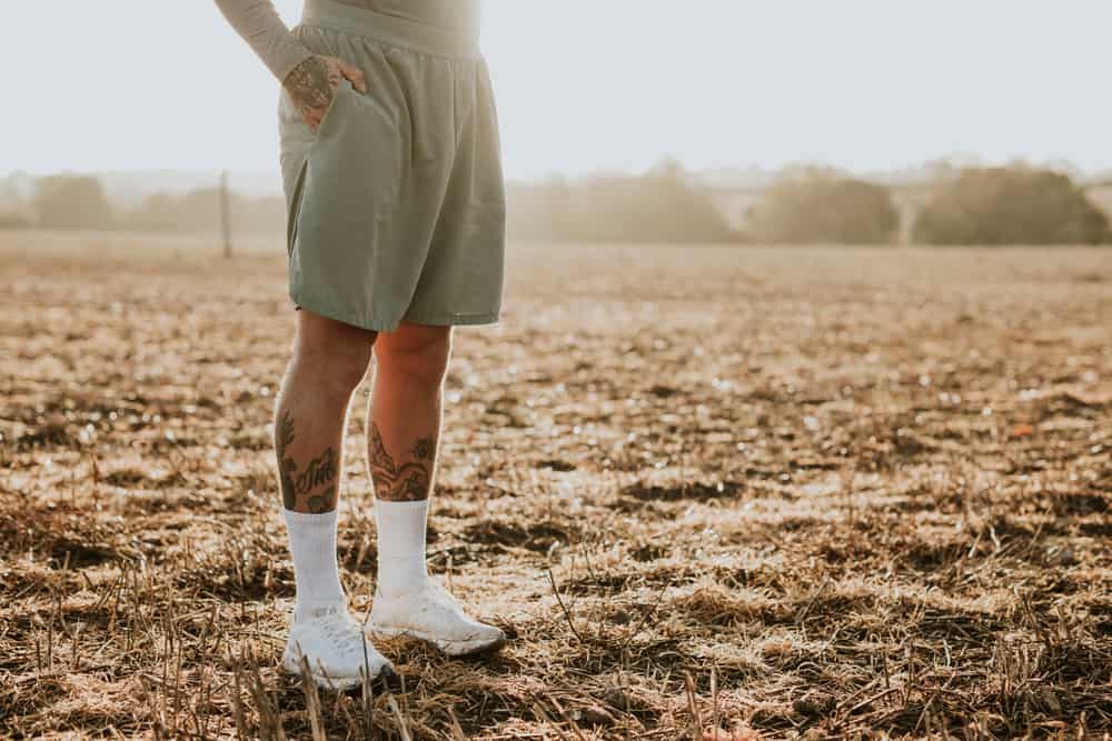 This is a close look at a tattooed man standing on a field wearing running shorts.