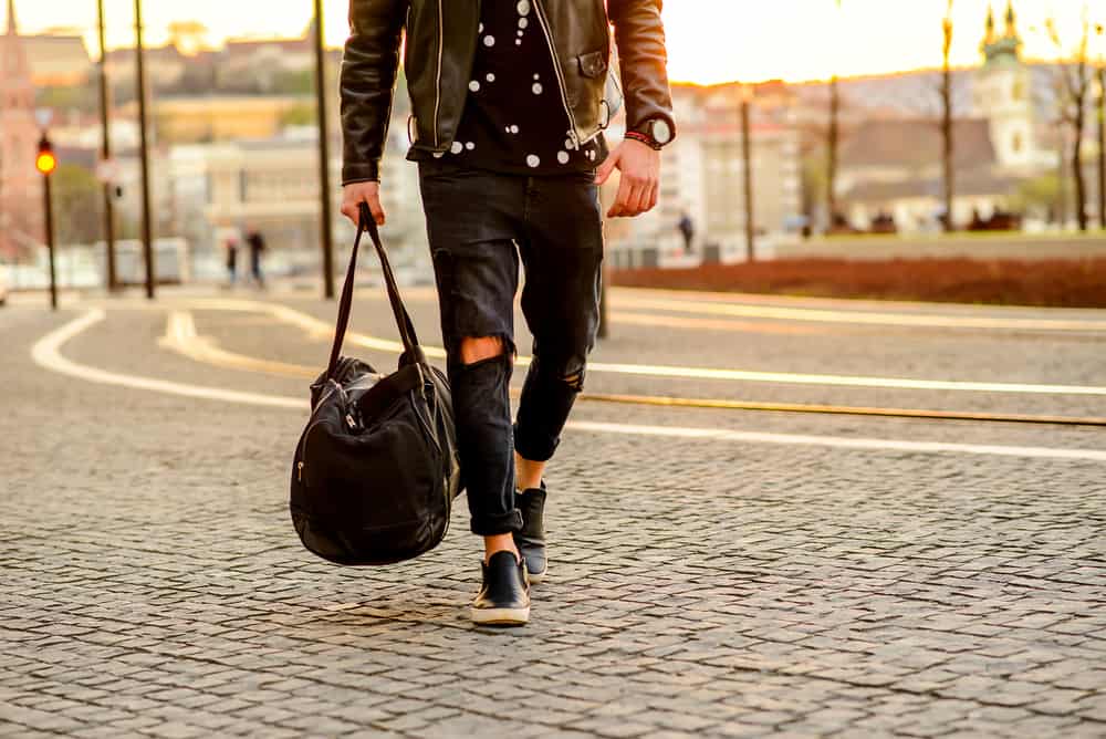 This is a man wearing a pair of ripped black jeans, black shirt and a brown leather jacket.