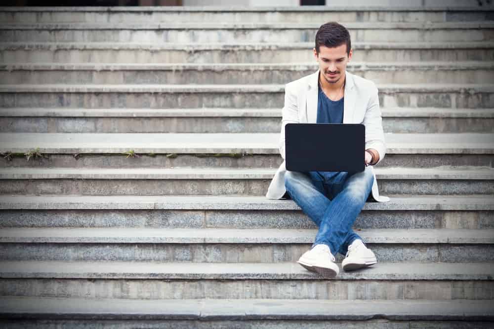 A man wearing jeans and blazer working on his laptop.