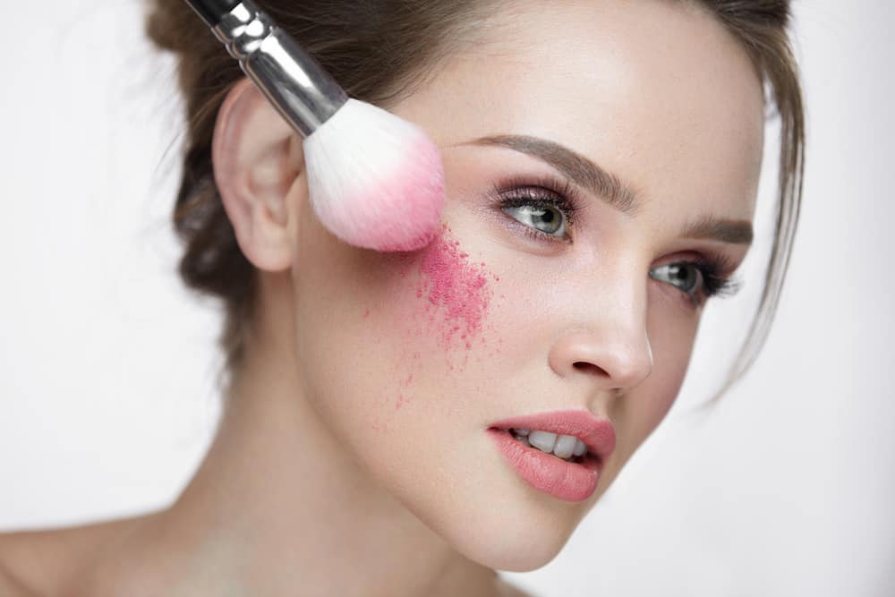 Woman applying loose blush using makeup brush.