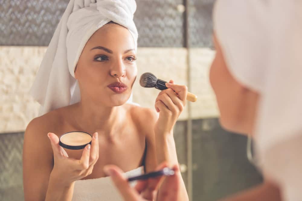 Woman in bath towel applying powder using a makeup brush.