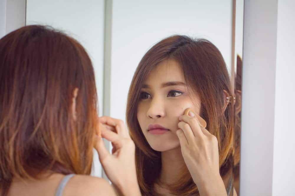 Woman applying powder puff foundation while looking at a mirror.