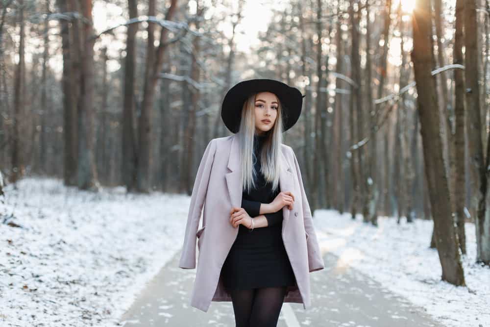 This is a woman wearing a little black dress while walking through a wintry forest.