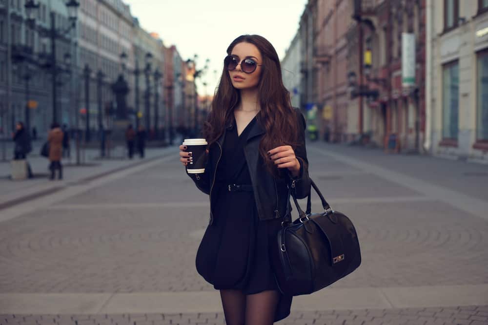 This is a woman wearing a little black dress with her black jacket and bag.