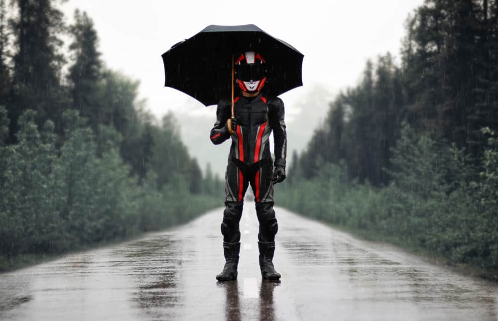 This is a rider with full gear standing under an umbrella.