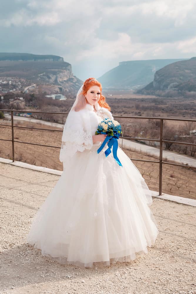 Red-haired bride in a large, princess-style gown holding a blue bouquet.